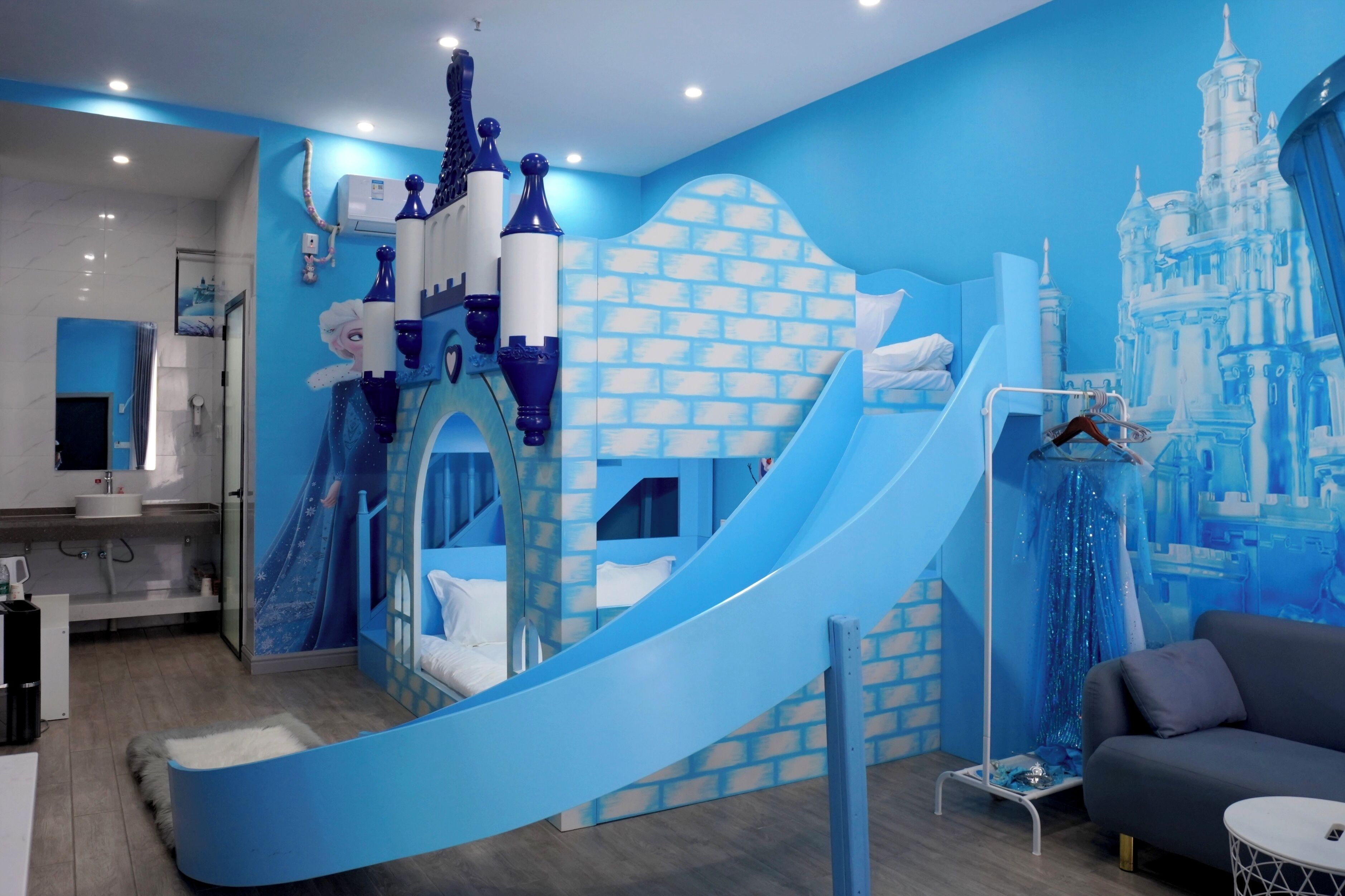 Zona de juegos infantiles con un tobogán, pared con motivos de castillo y un sofá.