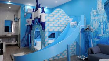 Zona de juegos infantiles con un tobogán, pared con motivos de castillo y un sofá.