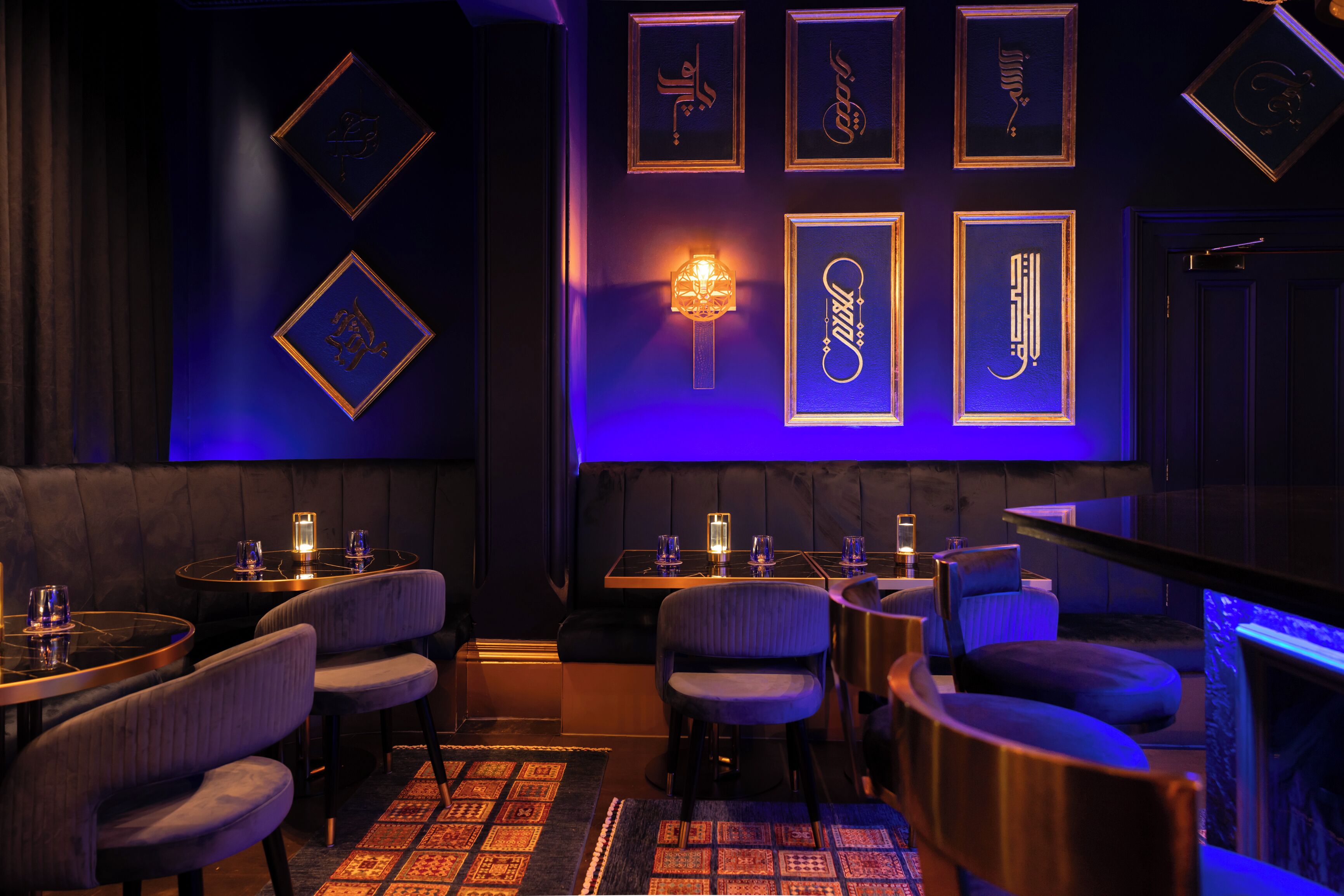 A dimly lit bar area with tables, chairs, and framed calligraphy art on the wall.