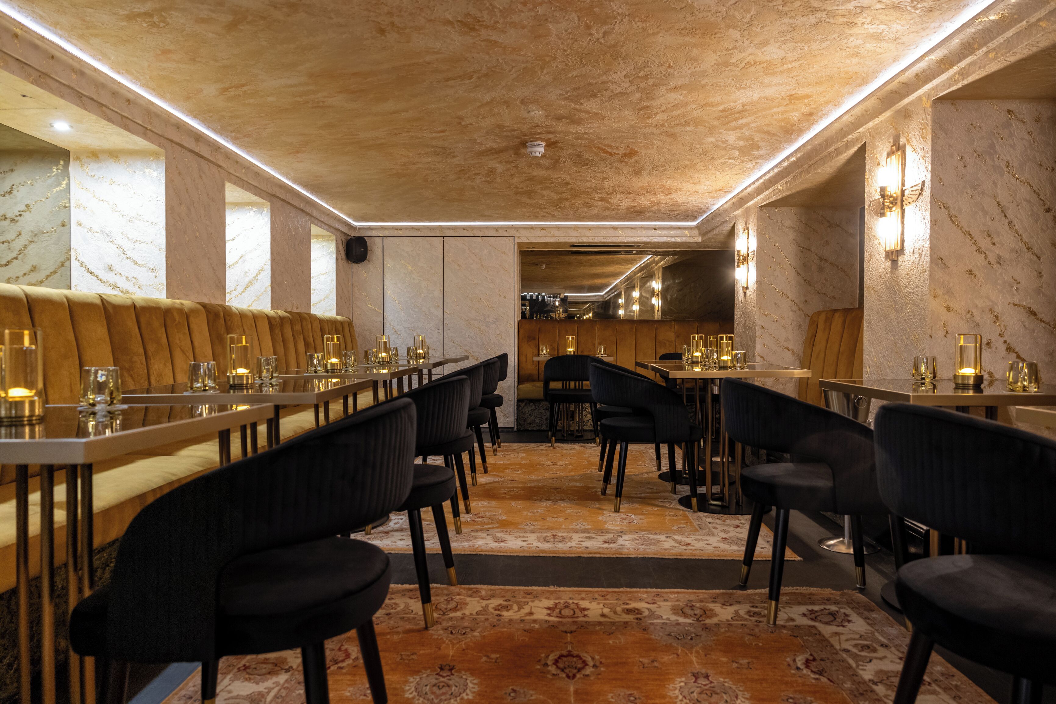 A restaurant with long tables, black chairs, and a patterned carpet.