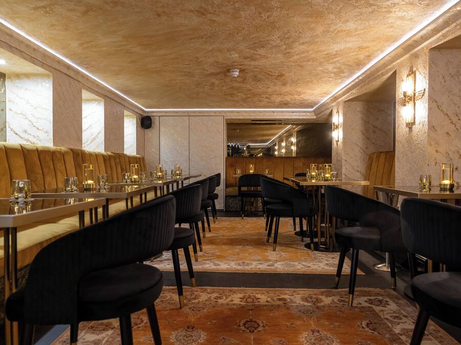 A restaurant with long tables, black chairs, and a patterned carpet.