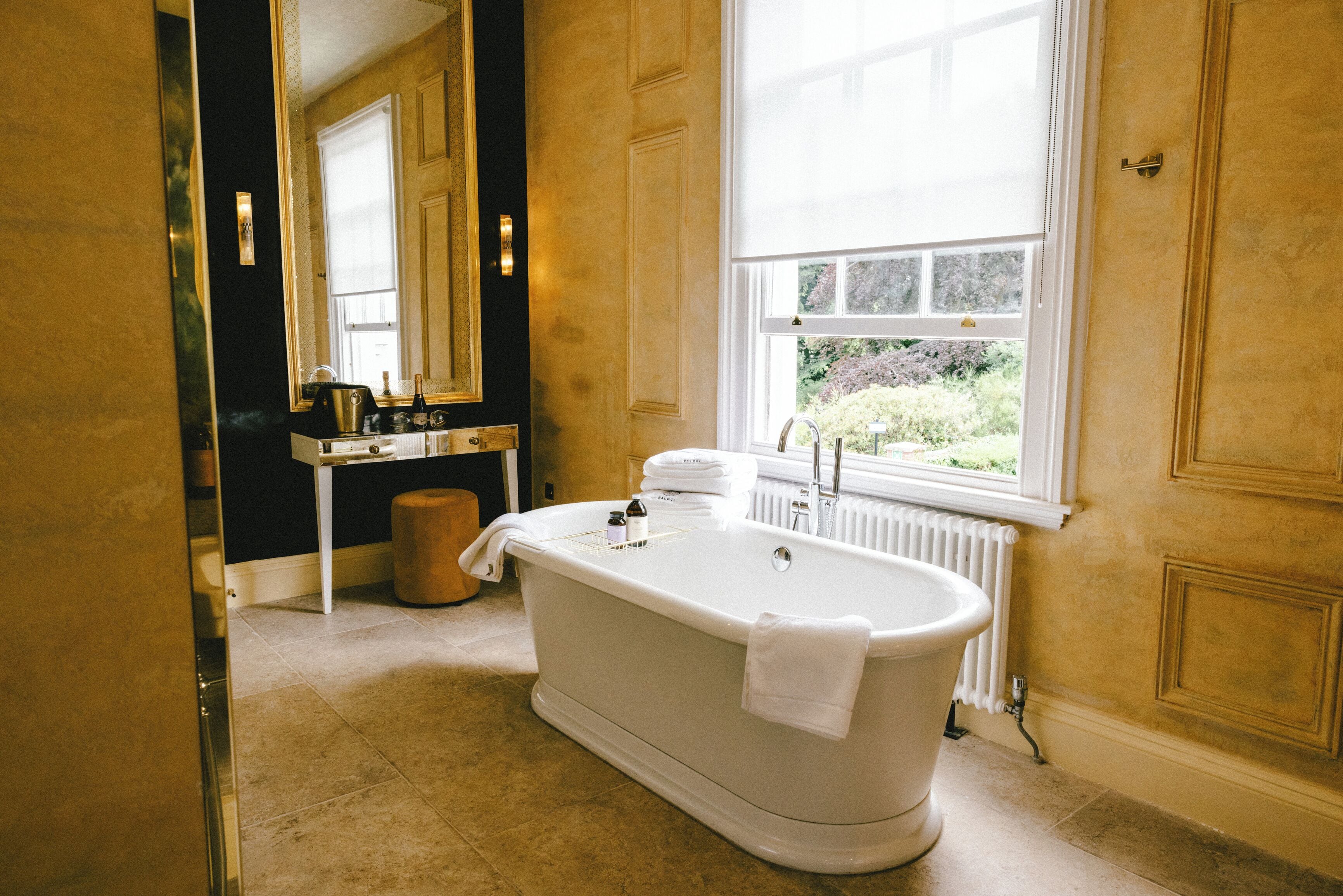 Une salle de bain avec une baignoire sur pieds, un meuble-lavabo avec un miroir et une fenêtre donnant sur la verdure à l’extérieur.
