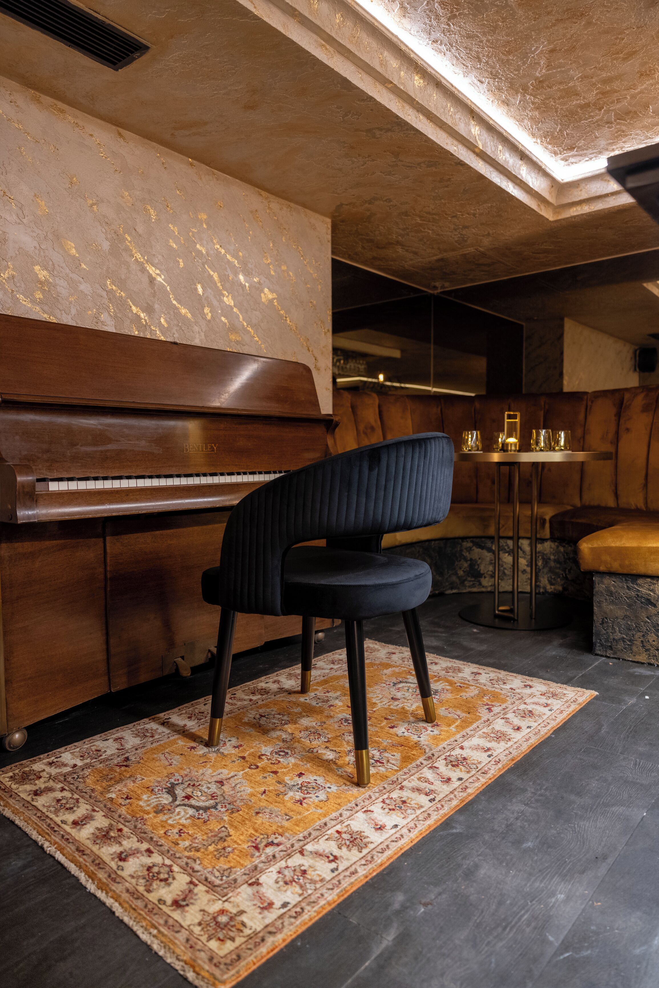A piano, a cushioned bench, a patterned rug, and a small table with candles.
