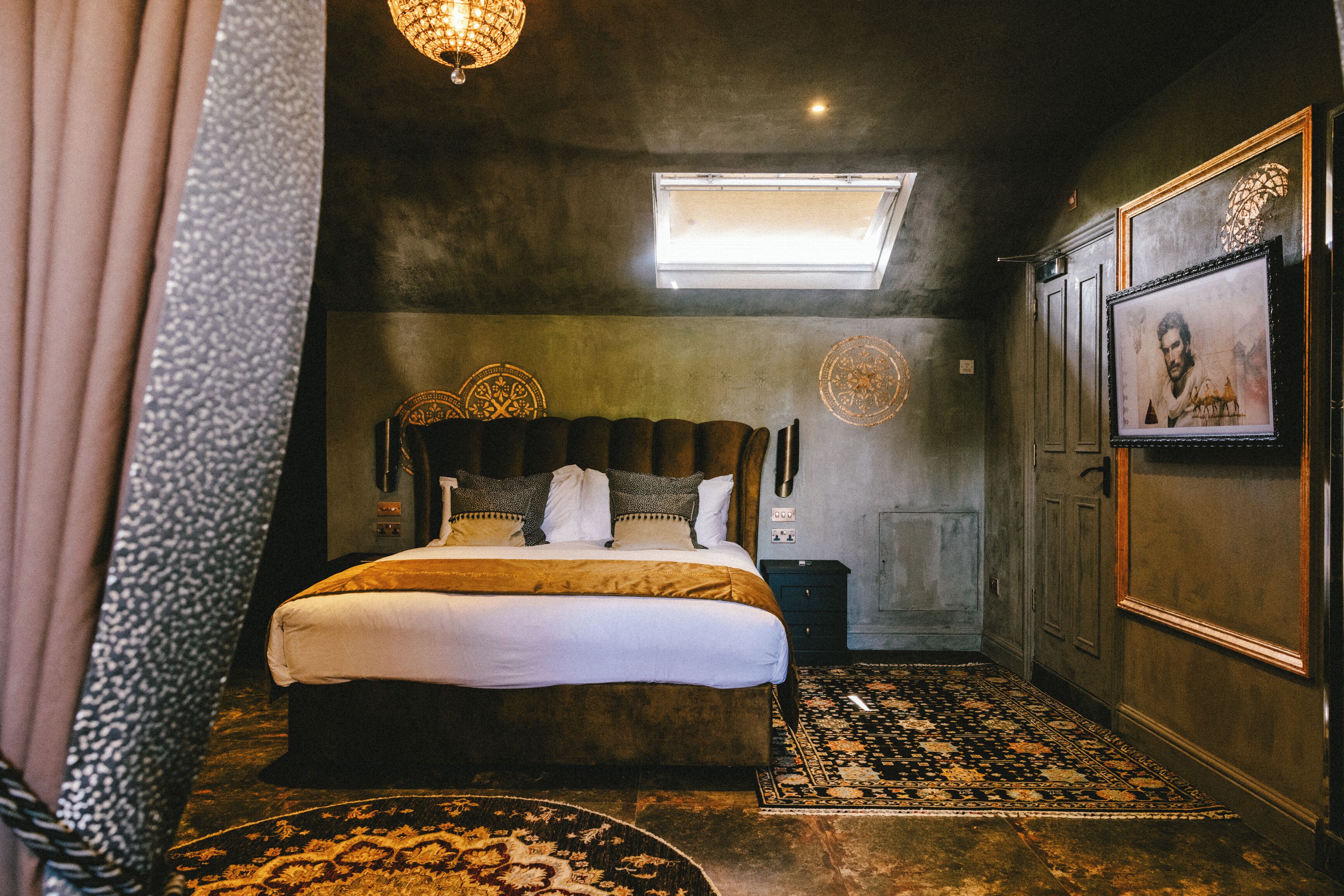 A bedroom with a large bed, a skylight, a patterned rug, and a framed picture on the wall.