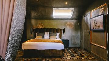 A bedroom with a large bed, a skylight, a patterned rug, and a framed picture on the wall.
