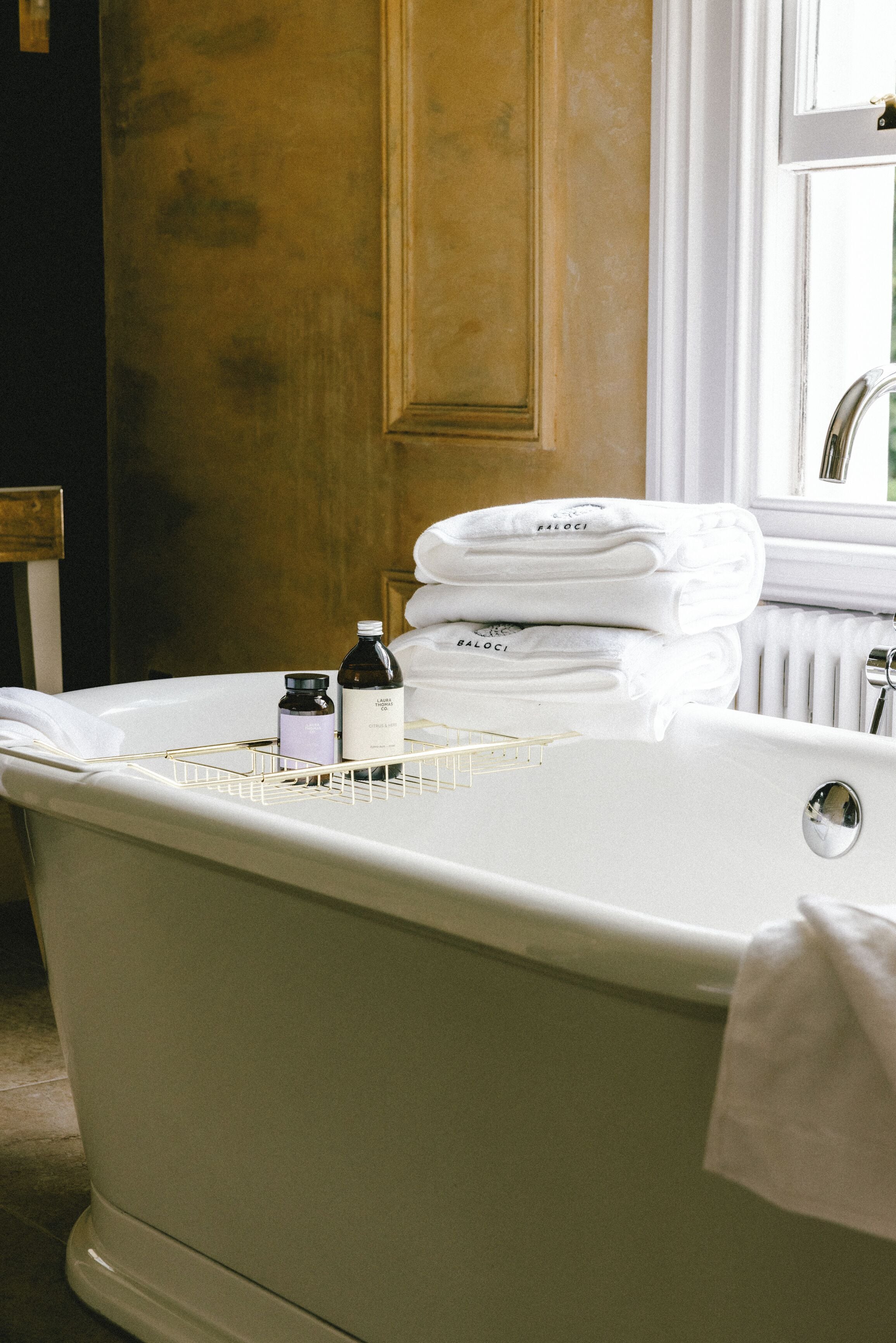 A bathroom with a white bathtub, a towel rack with folded towels, and a bottle on the edge of the tub.