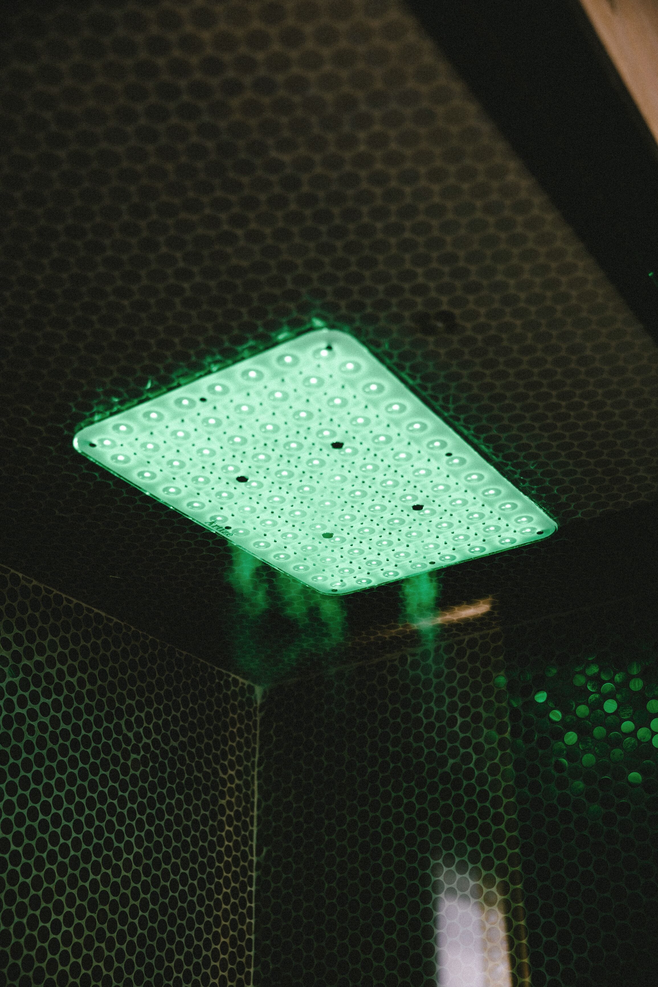 A ceiling with a square, perforated panel emitting green light.