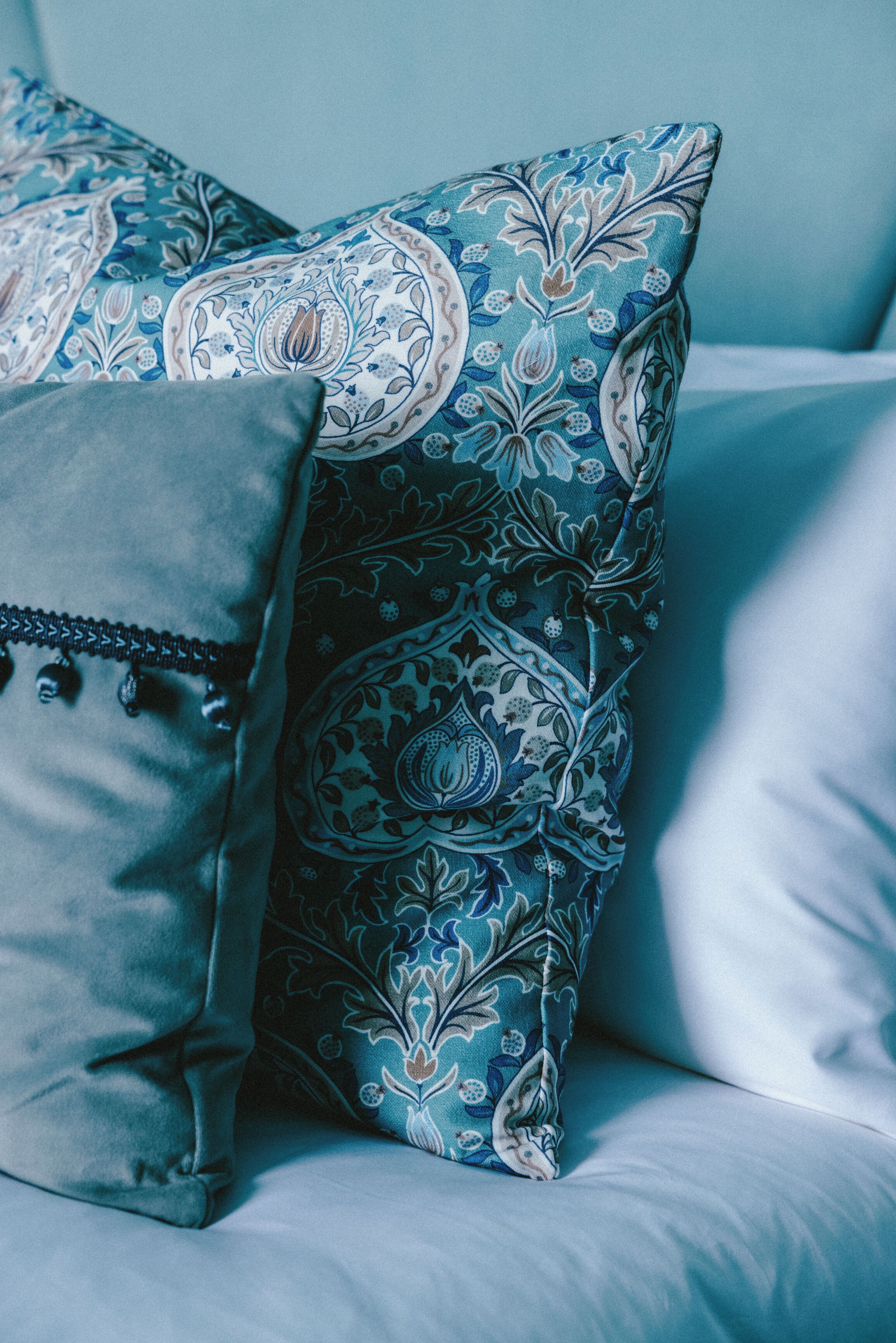 Una cama con almohadas de diseño azul y blanco y un cojín gris con flecos.