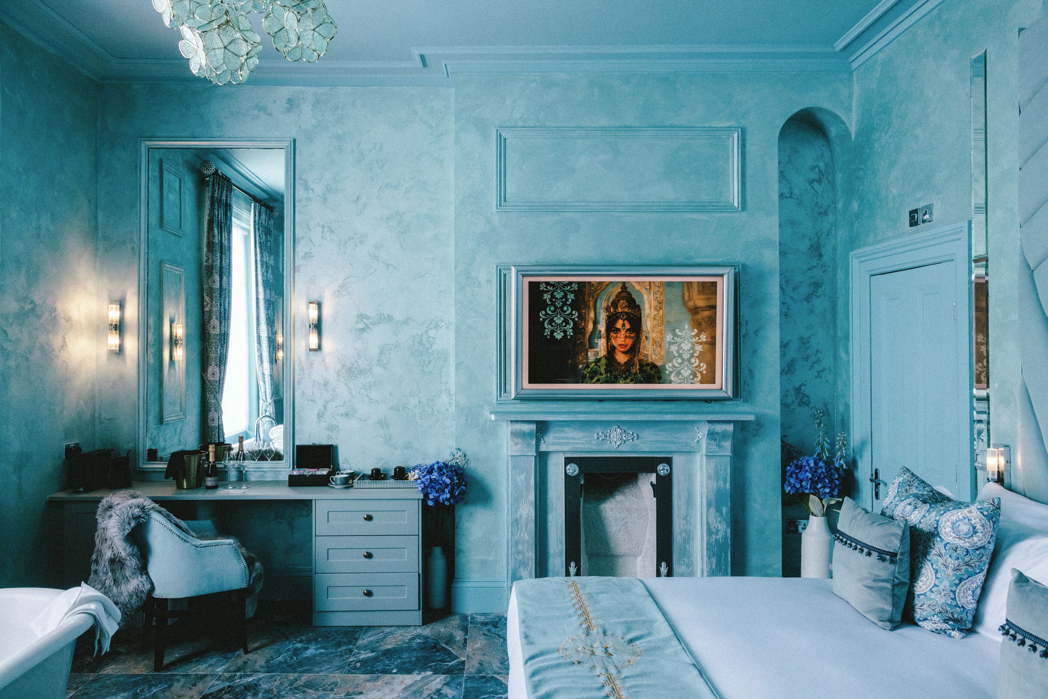 Een slaapkamer met een bed, een dressoir, een stoel, een open haard en een schilderij aan de muur.