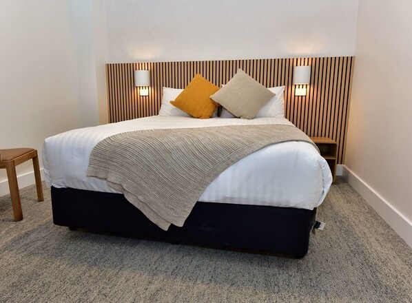 A neatly made bed with a wooden headboard, two bedside lamps, and a small wooden stool.