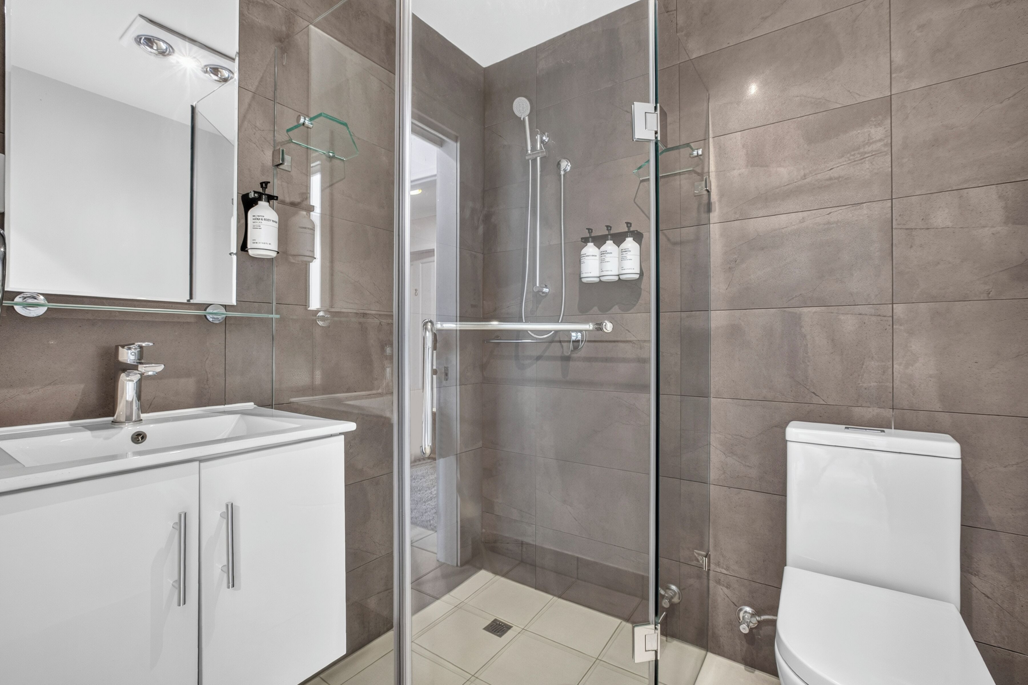 A modern bathroom with a glass-enclosed shower, a white sink, and a toilet.