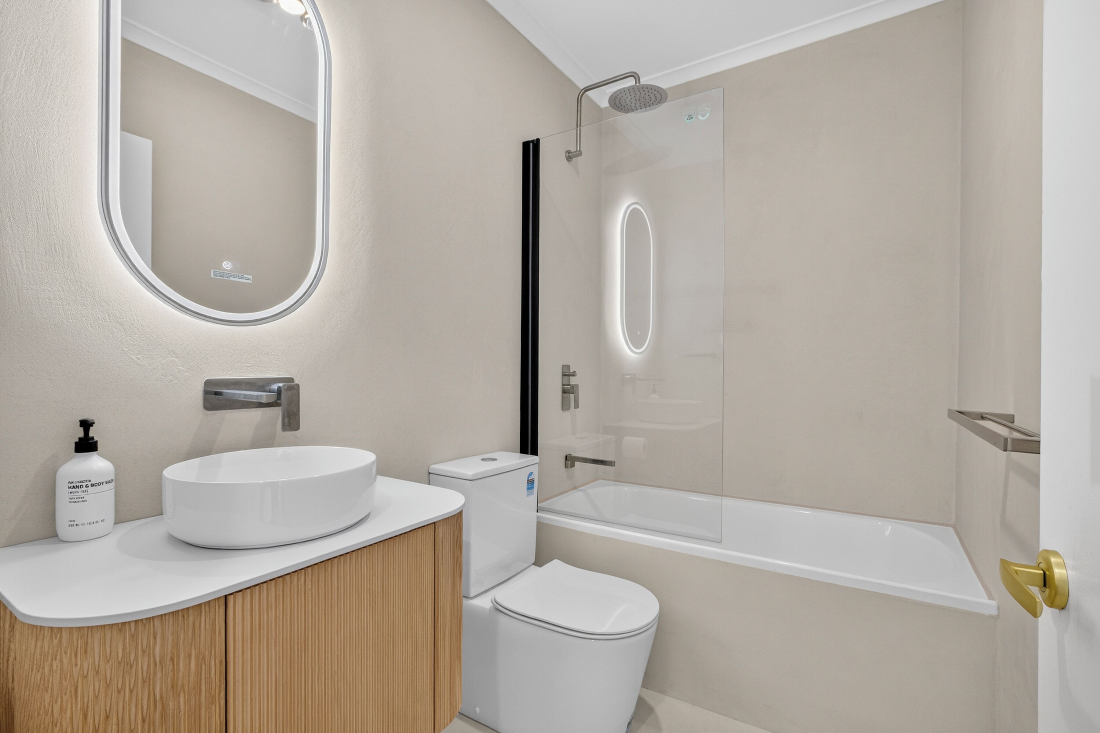 Un baño moderno con un espejo redondo, un lavamanos blanco, un inodoro y una ducha con cerramiento de vidrio.