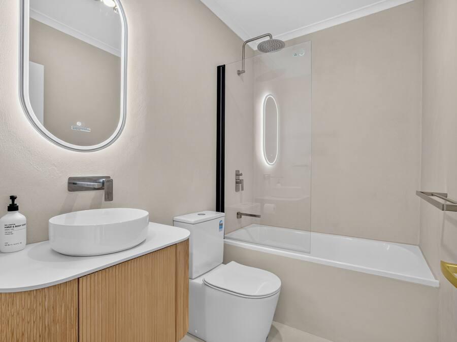 Un baño moderno con un espejo redondo, un lavamanos blanco, un inodoro y una ducha con cerramiento de vidrio.