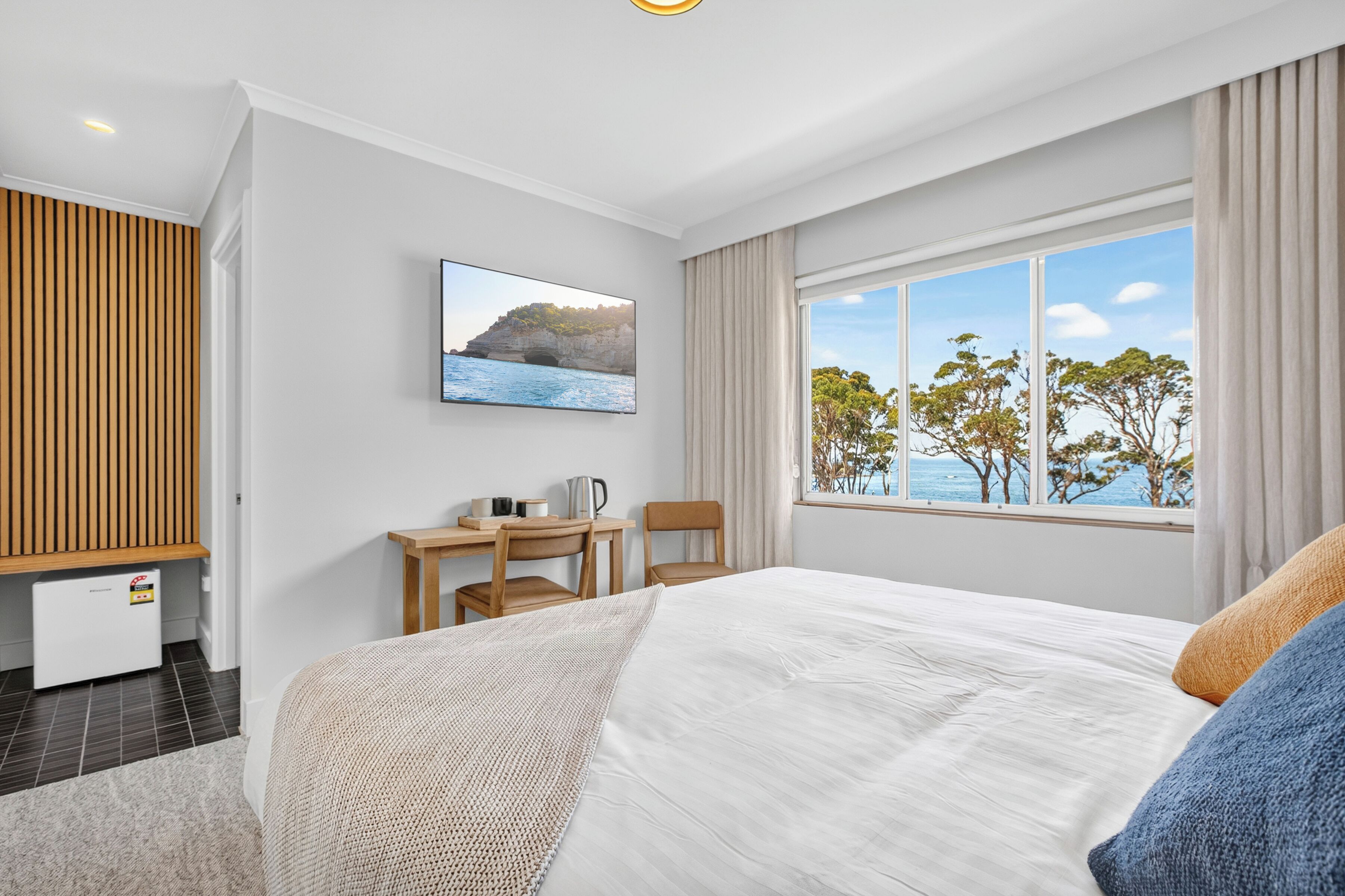 Ein Schlafzimmer mit Bett, Schreibtisch mit Stuhl, Fernseher und einem Fenster mit Meerblick.