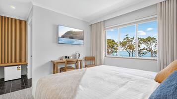 Ein Schlafzimmer mit Bett, Schreibtisch mit Stuhl, Fernseher und einem Fenster mit Meerblick.