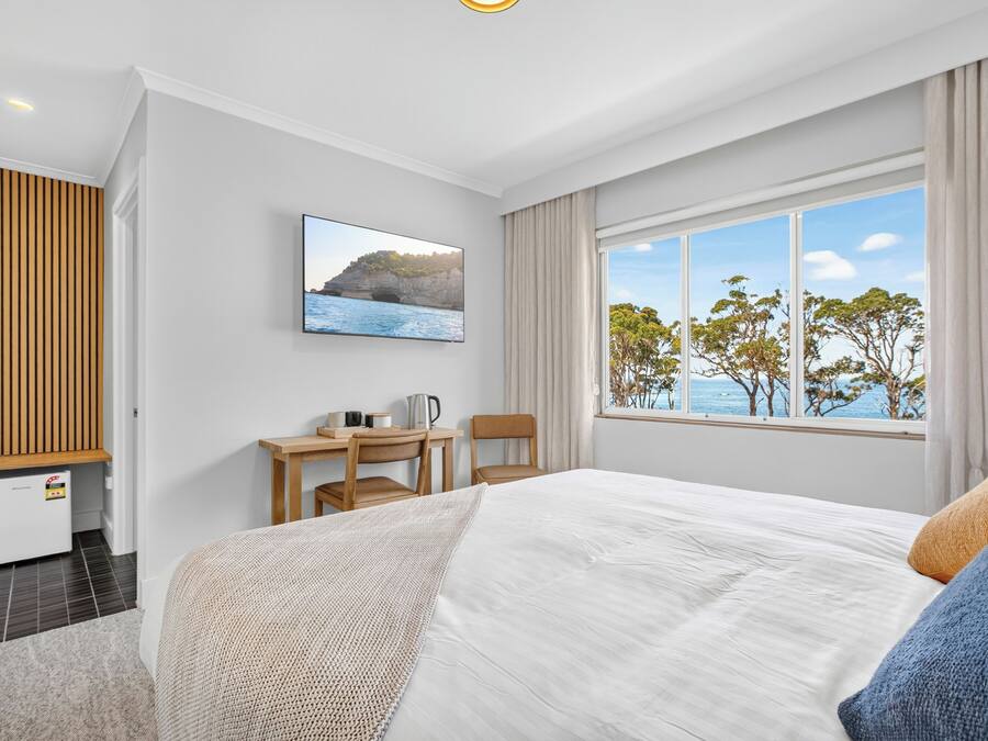 Ein Schlafzimmer mit Bett, Schreibtisch mit Stuhl, Fernseher und einem Fenster mit Meerblick.