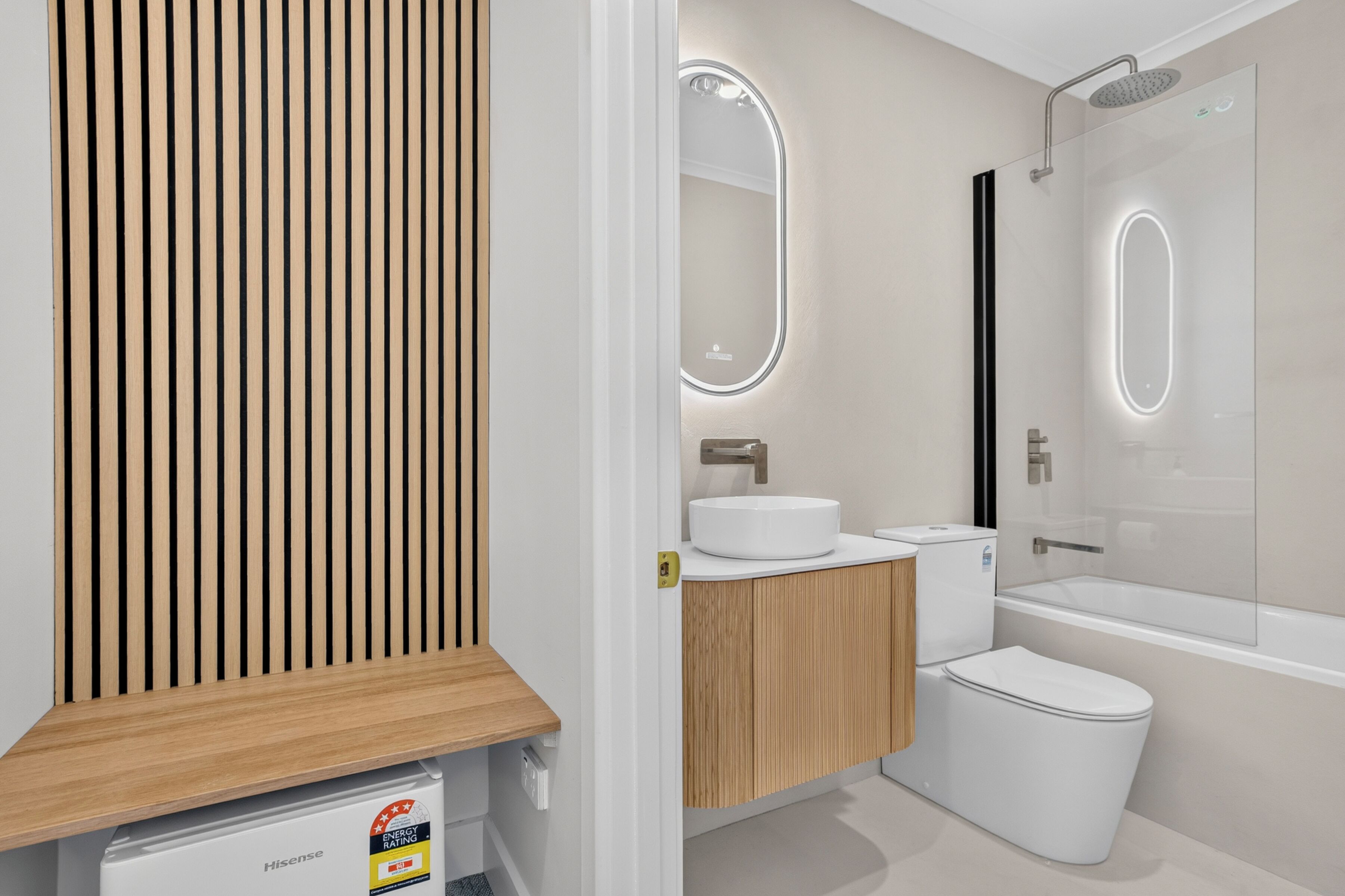 A modern bathroom with a wooden panel wall, a sink with a mirror, a toilet, and a bathtub.