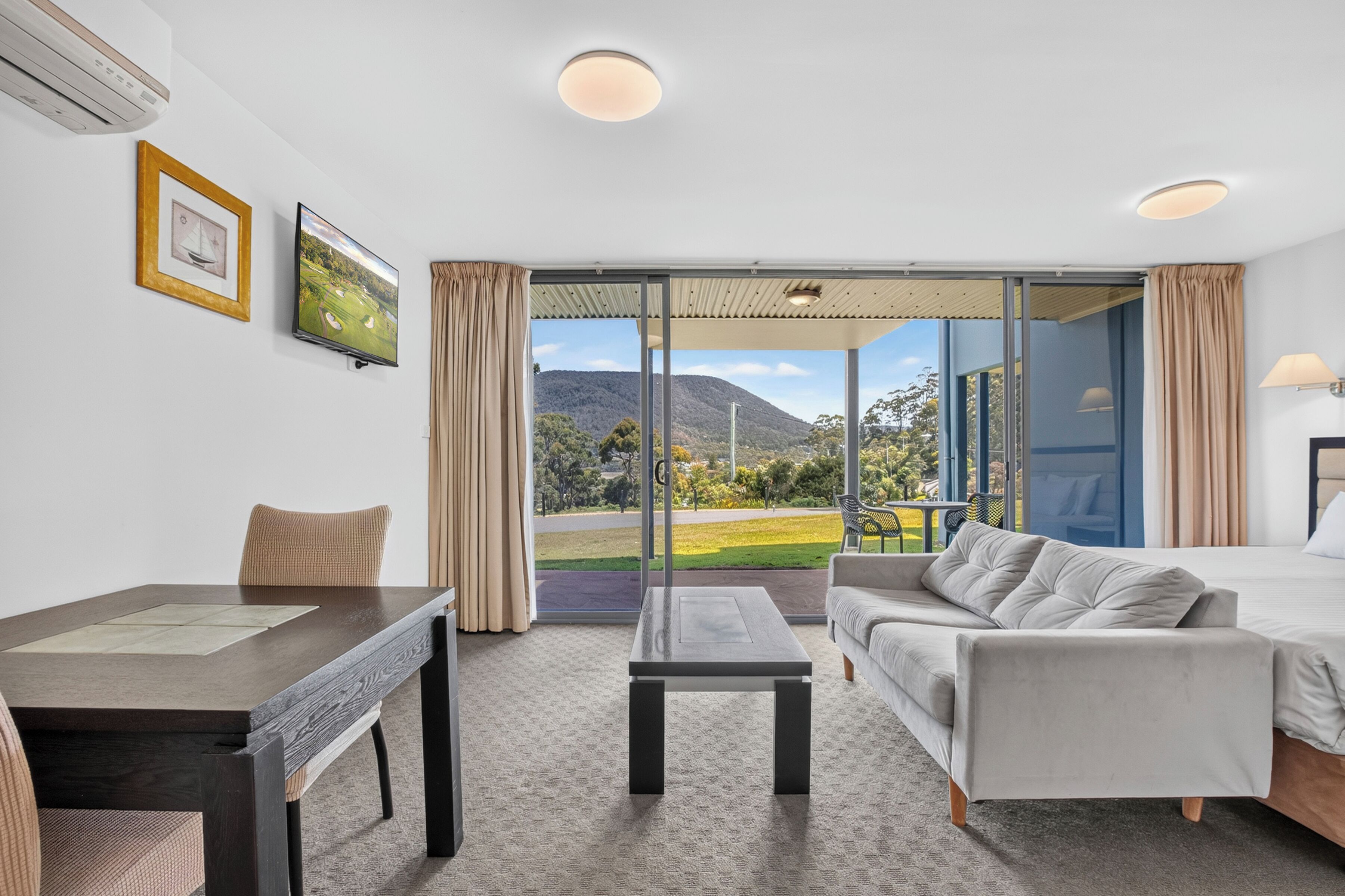 Habitación de hotel con cama, sofá, escritorio y vistas a un paisaje montañoso.