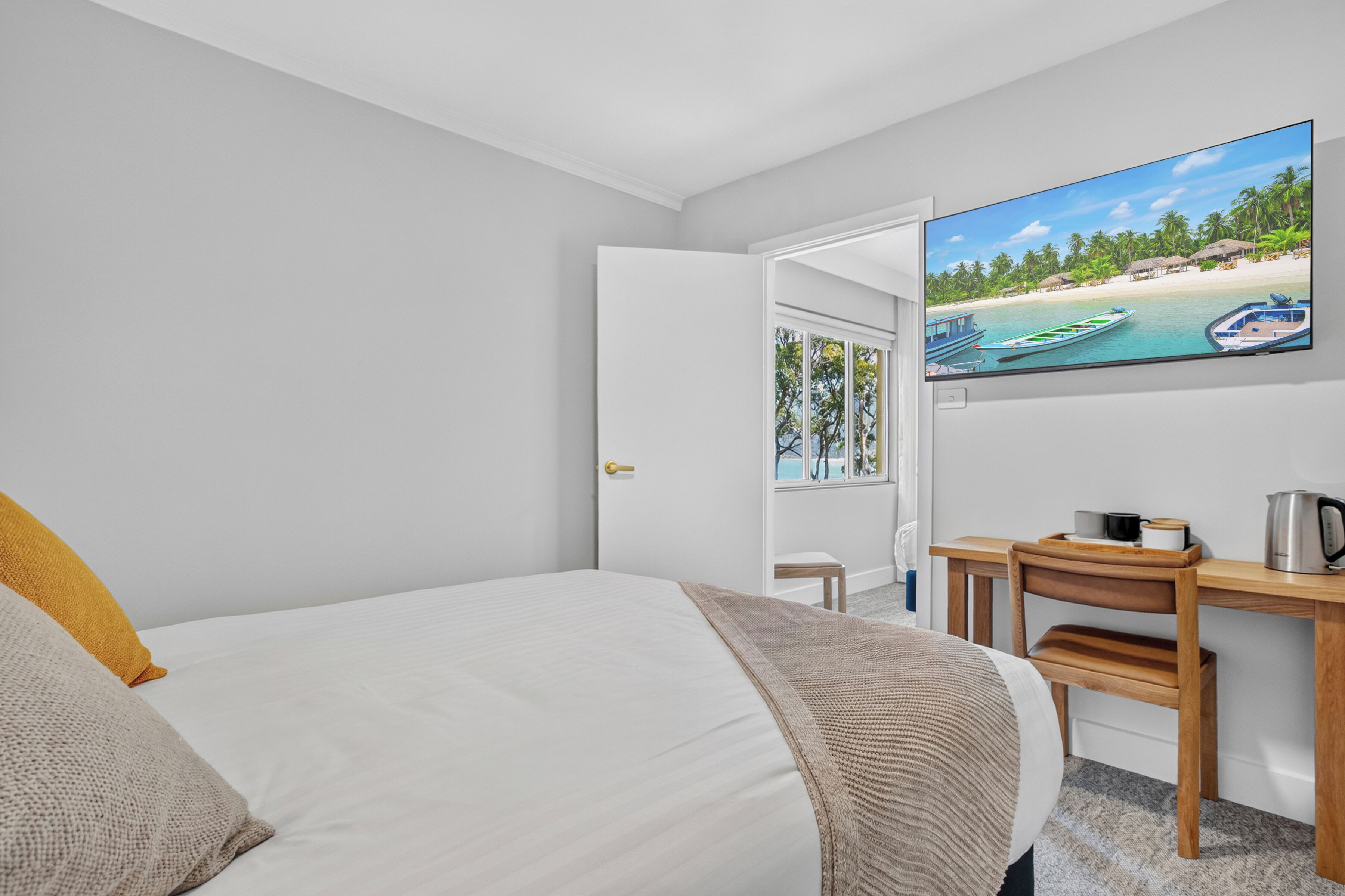 Habitació d'hotel amb llit, escriptori, cadira i televisió que mostra una escena de platja.