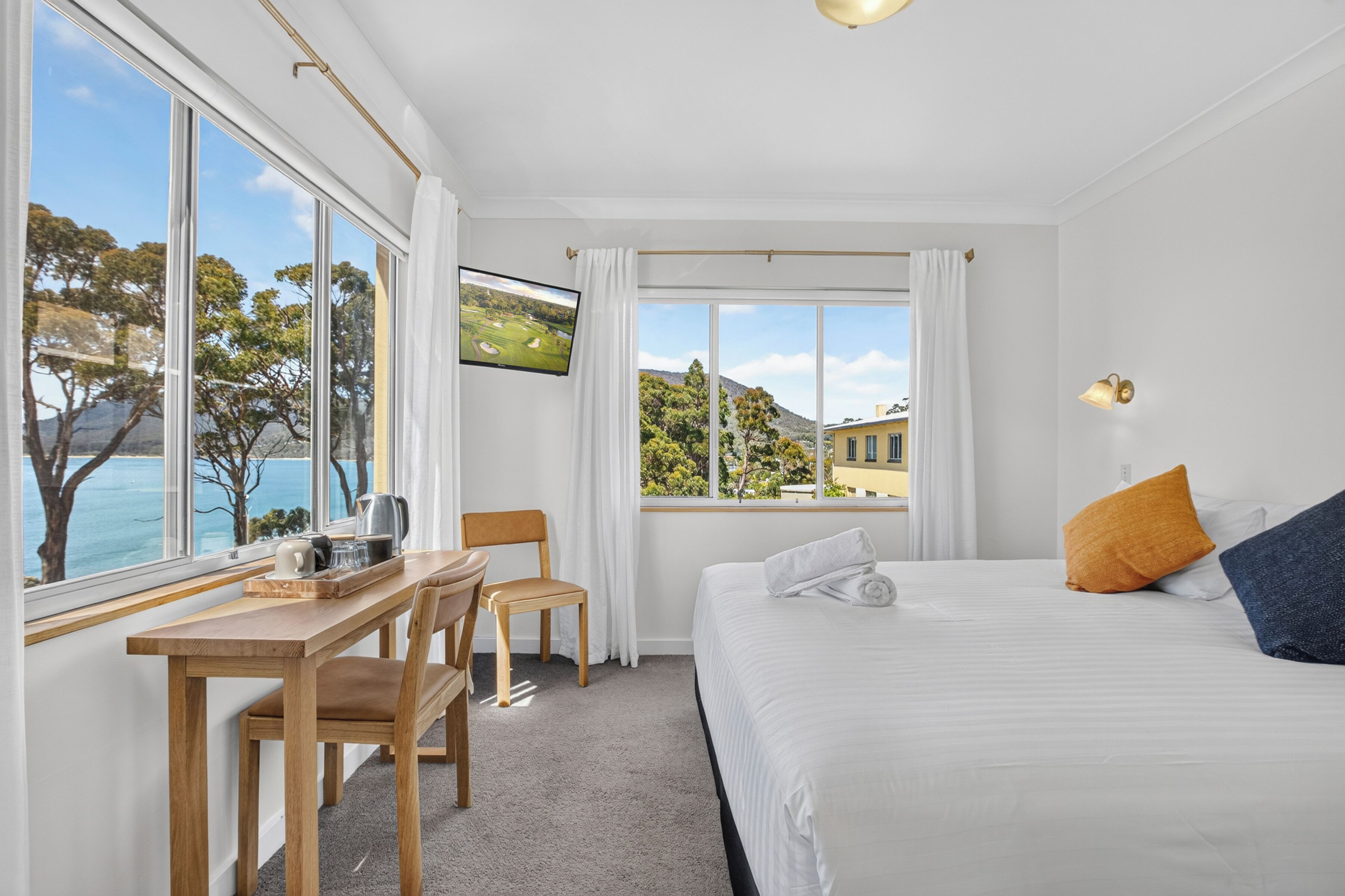 Habitación de hotel con cama, escritorio, silla, televisión y vistas al mar y colinas.