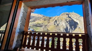 Uitzicht door een houten raam met balkon, op een bergachtig landschap onder een heldere lucht.