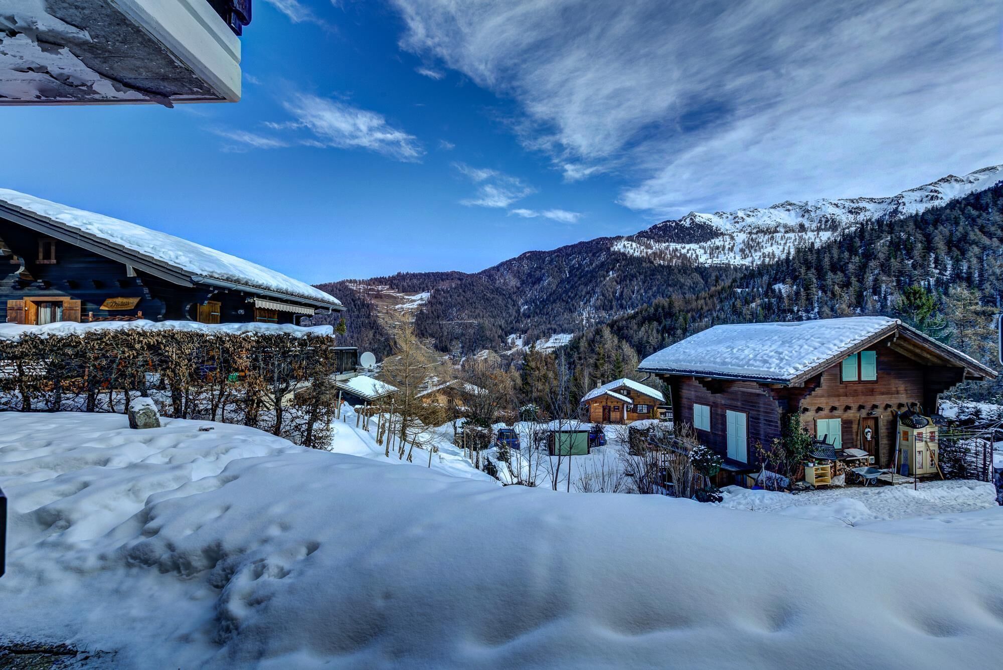 En snötäckt bergsby med trähus, en klar himmel och en dal.