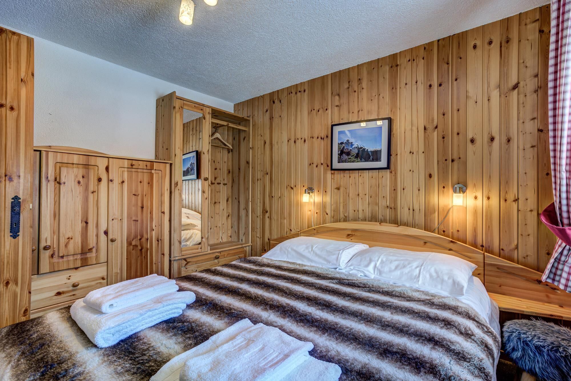 A wooden-paneled room with a bed, a wardrobe, and a mirror.