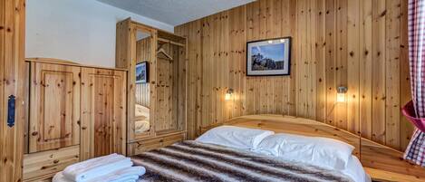 A wooden-paneled room with a bed, a wardrobe, and a mirror.