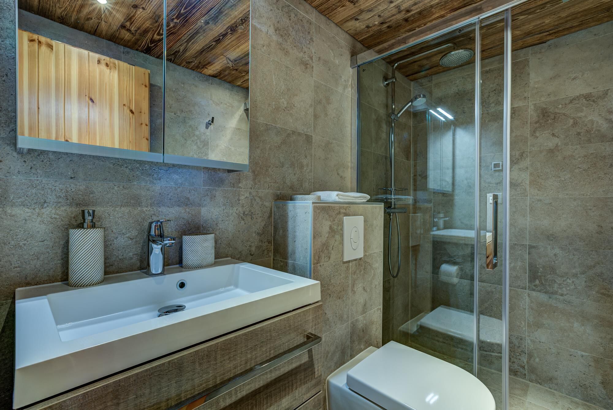 A modern bathroom with a large sink, a glass shower enclosure, and wooden ceiling accents.