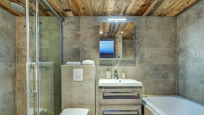 Et badeværelse med en brusekabine med glasvægge, et hvidt toilet, en vask med et spejl over, og et badekar.