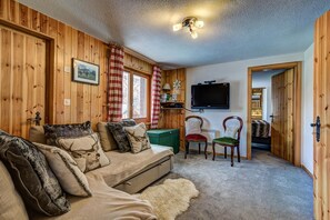 A cozy cabin interior with a sofa, chairs, a television, and a wooden wall.