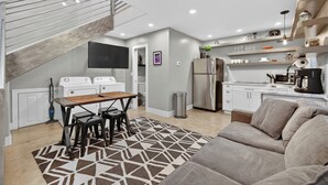 Una cucina moderna con elettrodomestici bianchi, un'area pranzo con tavolo e sedie, un divano e una scala che conduce a un piano superiore.