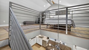 Camera mansarda in stile loft con letto a castello, un angolo cottura e una poltrona sospesa.