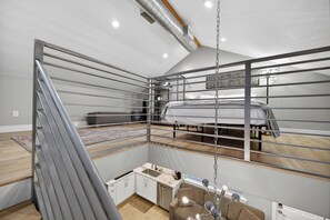 Quarto estilo loft com beliche, pequeno espaço de cozinha e cadeira suspensa.