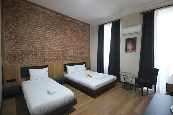 A hotel room with two beds, a brick wall, a small table, a chair, and a painting on the wall. - Linada Hotel Taksim (Istanbul)