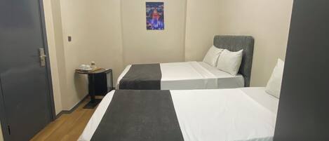 A hotel room with two beds, a small table, a wall-mounted picture, and a modern light fixture.