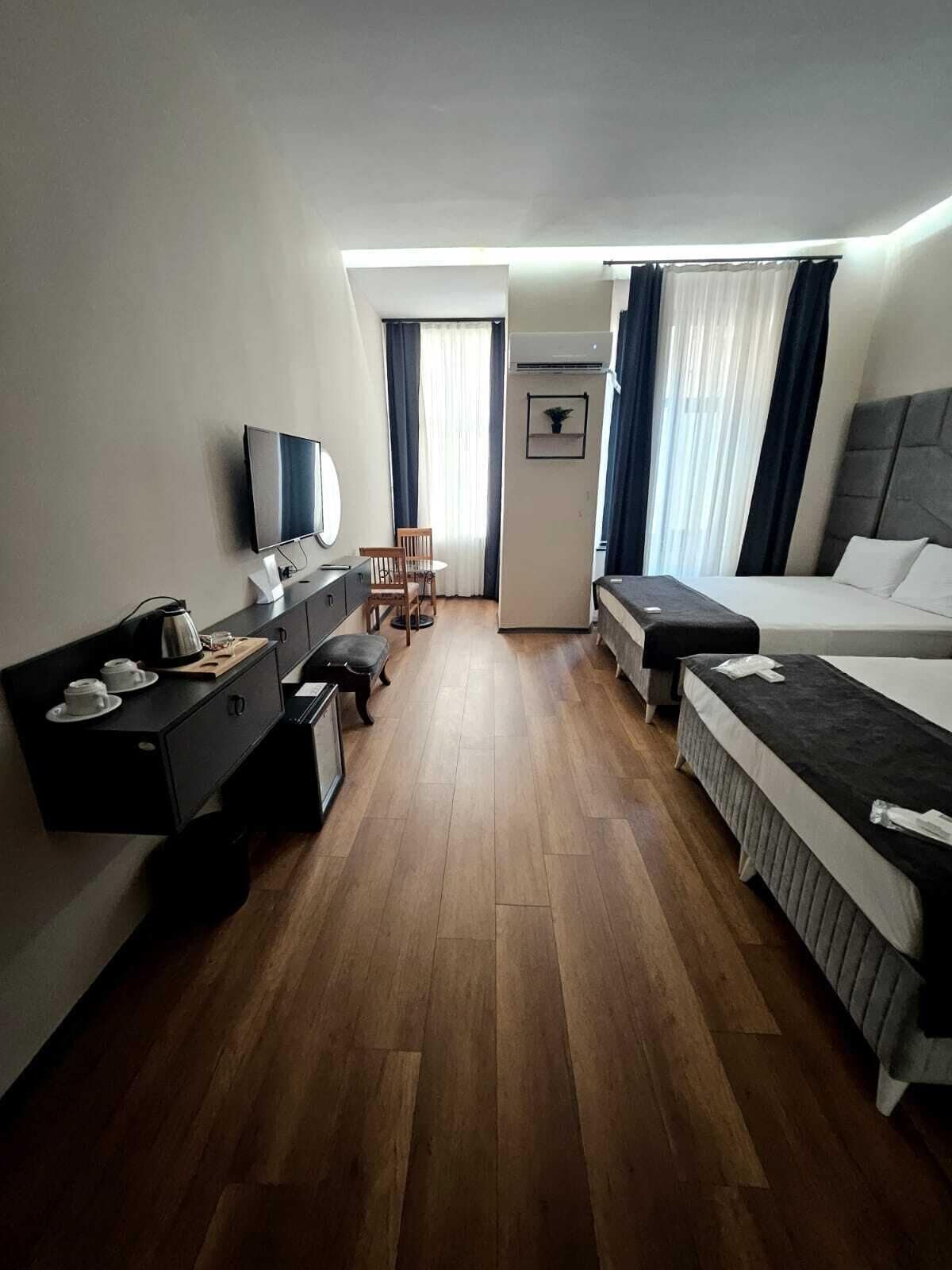 A hotel room with a bed, a desk with a computer, a chair, a TV, and a small table with cups.
