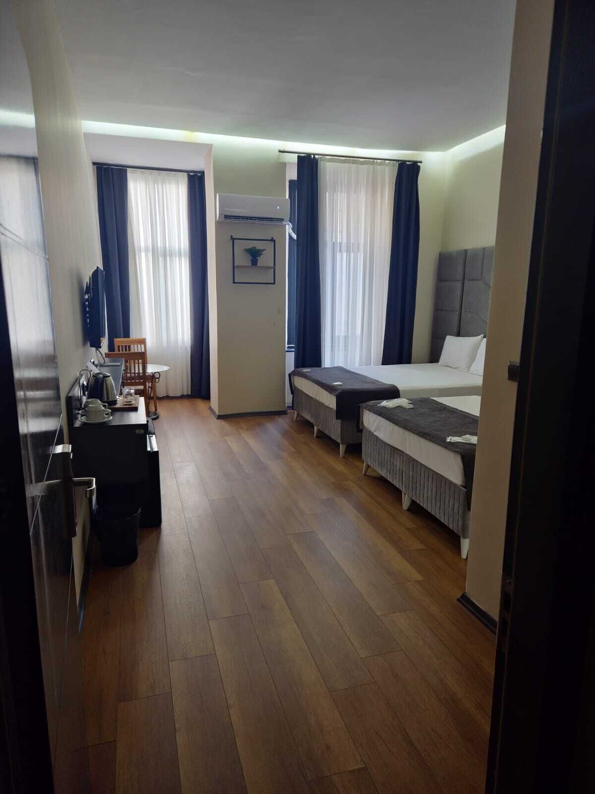 A hotel room with a bed, a desk, a chair, a small table, and a kitchenette.