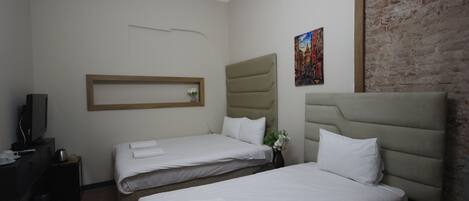 Quarto de hotel com duas camas, televisão, uma mesinha e parede de tijolos.