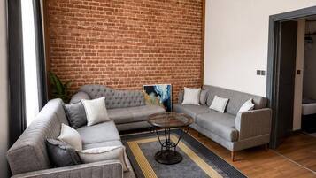 A modern living room with a brick accent wall, grey sofas, a coffee table, and a patterned rug.