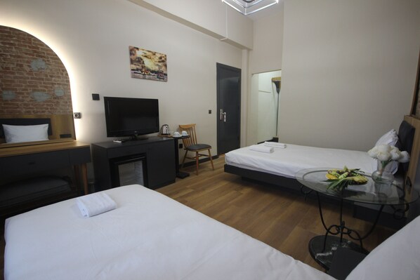 Habitación de hotel con dos camas, un escritorio con computadora, un televisor y una pequeña mesa con flores.