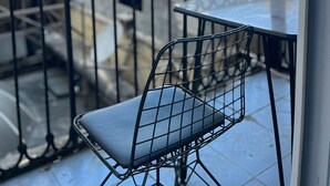 Een balkon met een metalen stoel en tafel, met uitzicht op een stadsbeeld met gebouwen en een heldere lucht.