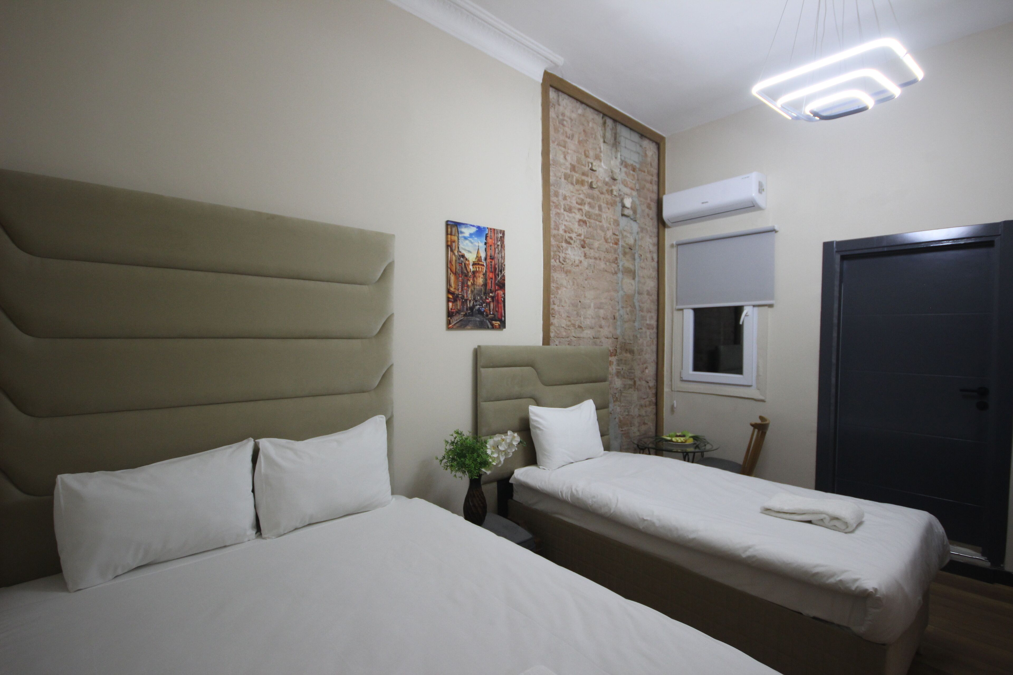 Una camera d'albergo con due letti, un muro in mattoni, un condizionatore d'aria e una porta.
