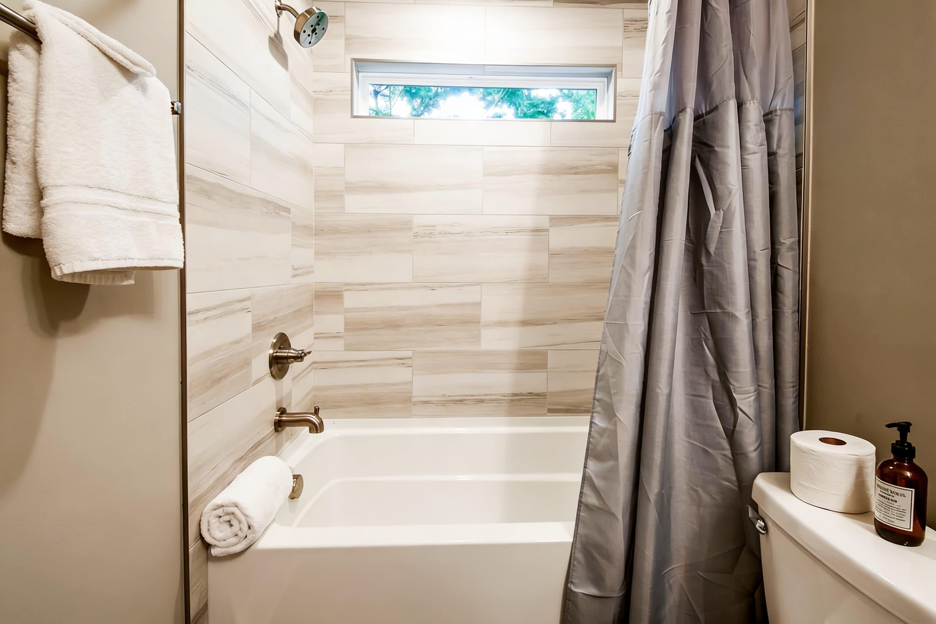Un baño con bañera, ventana y un inodoro con una botella de jabón para manos.