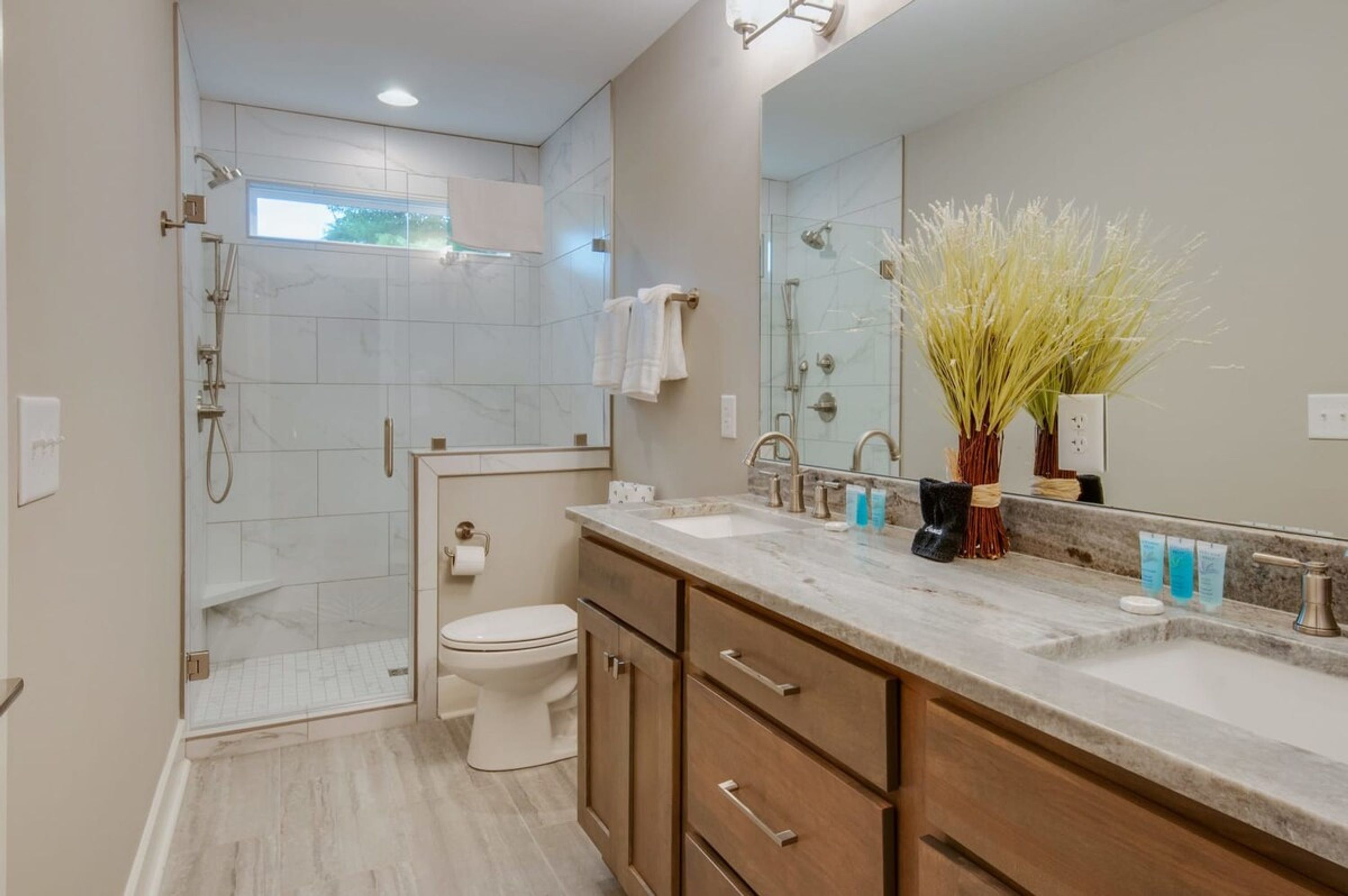 Un baño moderno con ducha a ras de suelo, inodoro, lavabo con un espejo grande y armarios de madera.