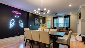 A modern living room with a dining area, featuring a black wall with neon signs, a chandelier, and a ceiling fan. - Booking Fast 12 Beds-large Yard (Nashville)