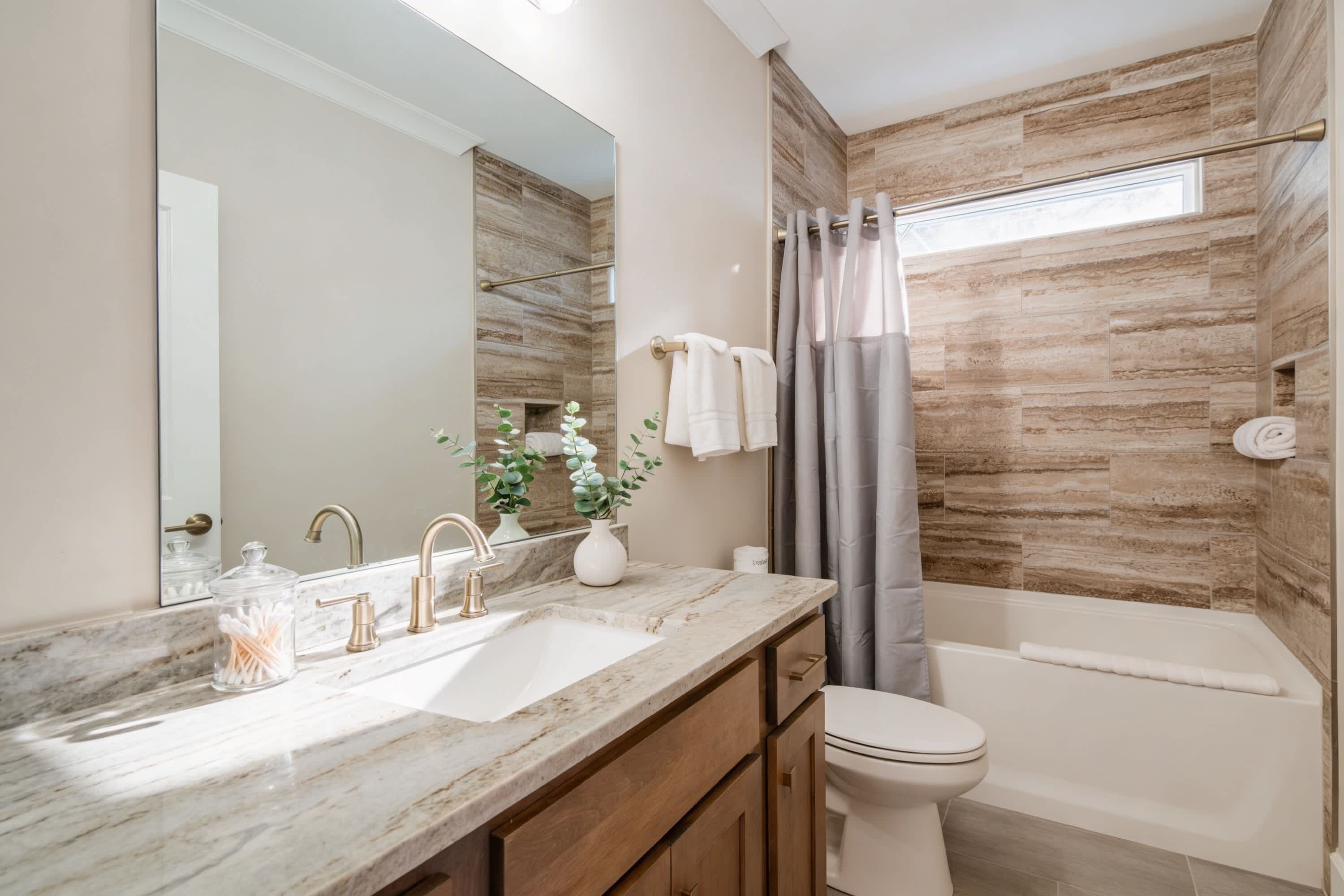A modern bathroom with a marble vanity, a toilet, and a bathtub.