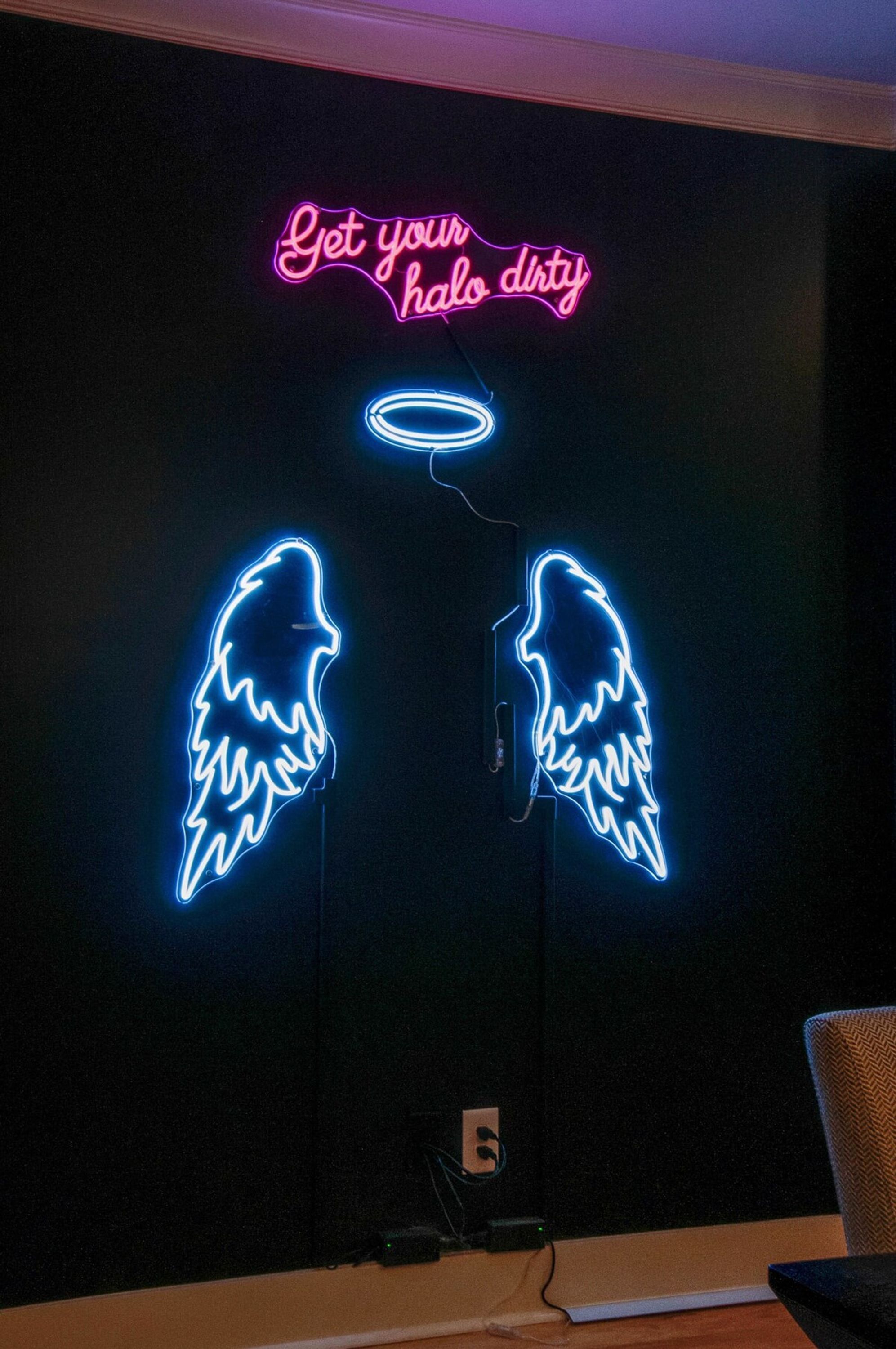 Une enseigne au néon avec l’inscription « Salissez votre auréole » et deux néons en forme d’ailes.