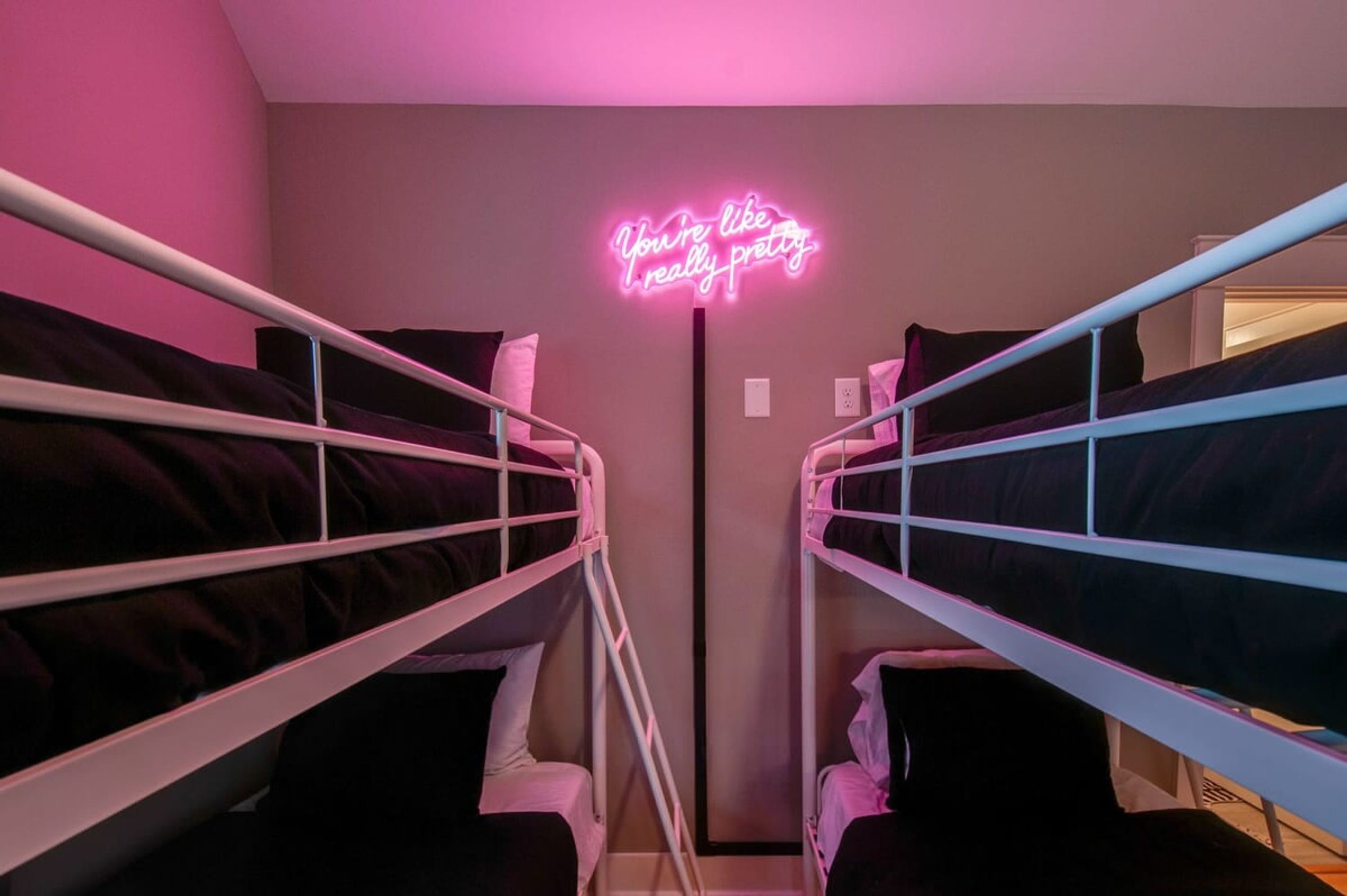 A room with bunk beds, a neon sign on the wall, and a door in the background.
