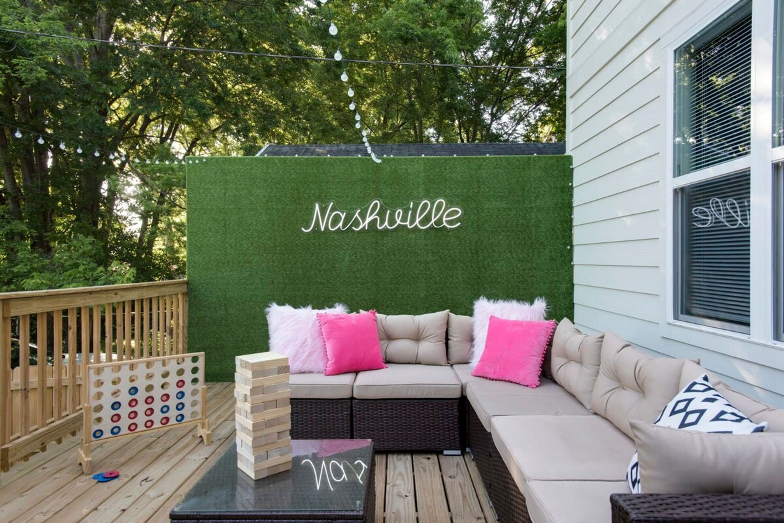 Una terraza con un muro verde, un sofá con almohadas rosadas y una mesa de madera con un cartel.